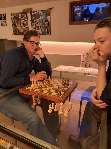Two individuals are engrossed in a game of chess on a glass table, illuminated by warm indoor lighting